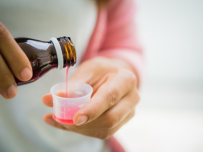 Closeup woman pouring medication or antipyretic syrup from bottle to cup. Healthcare, people and medicine concept -
