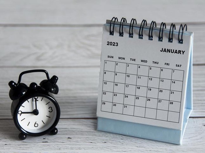 January 2023 white desk calendar with black alarm clock pointing at 9 oclock on wooden table. Calendar concept