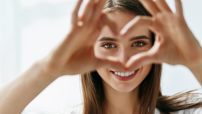 Healthy Eyes And Vision. Portrait Of Beautiful Happy Woman Holding Heart Shaped Hands Near Eyes. Closeup Of Smiling Girl With Healthy Skin Showing Love Sign. Eyecare. High Resolution Image
