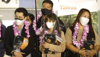 Rombongan pertama wisatawan asing memegang suvenir setelah tiba di Bandara Internasional Taoyuan di Taoyuan, Taiwan Utara. Pengunjung tidak lagi diharuskan untuk dikarantina saat masuk, atau mengikuti tes PCR apa pun. AP/Chiang Ying-ying