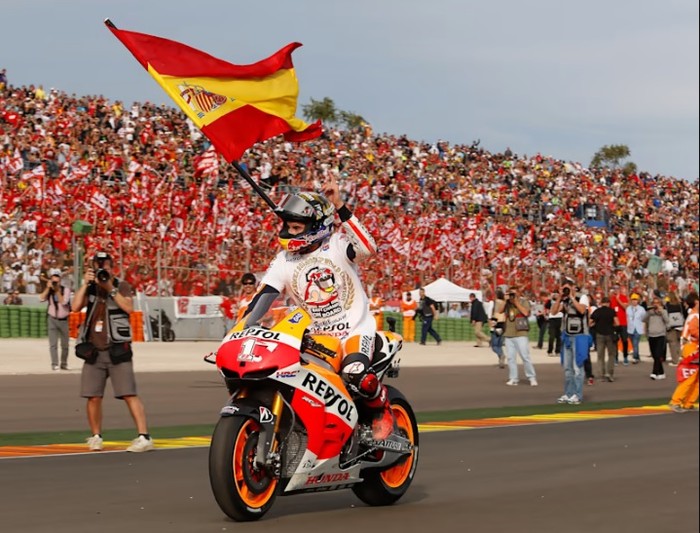 Marc Marquez memegang bendera Spanyol di lintasan.