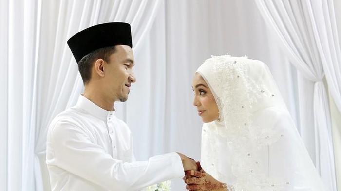 A Muslim young woman holding a young mans hand for salam (gesture of mannerism in greeting) when they are certified newlywed in Islam akad nikah (solemnisation) ceremony. In this ceremony, newlywed and all guests are required to wear pure white tradiitonal clothing.