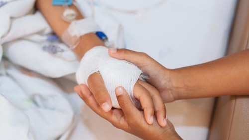 Child girl holding sick young sister hand who have IV solution bandaged with love and care in the hospital