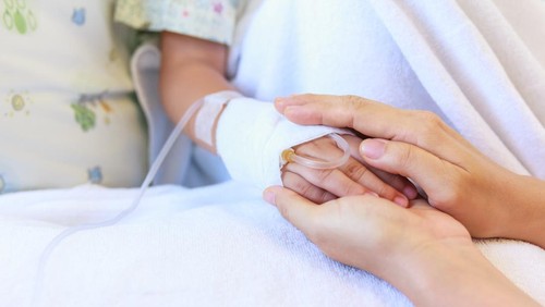 Close up hand of parent holding hand of child in hospital, saline intravenous (IV) on hand, shallow depth of field (DOF) saline intravenous (IV) in focus.