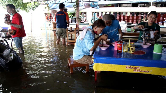 A boy plays with water in a bag as customers are seen in a flooded noodle shop at the banks of Tha Chin river in Nakhon Pathom, in the outskirts of Bangkok, Thailand October 15, 2022. REUTERS/Juarawee Kittisilpa