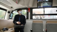 Tampak penumpang di dalam bus yang sedang memainkan laptop. Terlihat di dalam bus tersebut terdapat televisi untuk menunjukkan peta.
