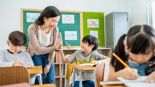 Pupil boy hi five with teacher in classroom at elementary school. Student boy studying in primary school. Children writing notes in classroom. Education knowledge, successful teamwork concept