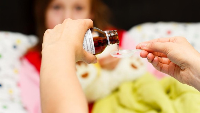 Mother pouring tasty syrup to ease her little girls cough.