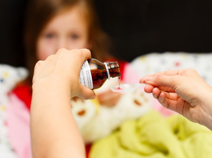 Mother pouring tasty syrup to ease her little girls cough.