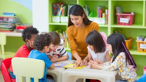 Asian female teacher teaching mixed race kids reading book in classroom,Kindergarten pre school concept