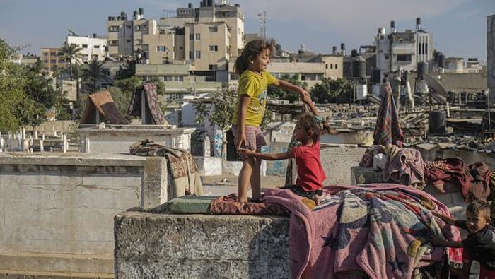 Miris, Banyak Tunawisma di Palestina Tinggal di Kuburan GAZA, PALESTINE - 2022/10/19: Palestinian children from the Kahil family play in front of their home in the Sheikh Shaaban cemetery in Gaza City. There is a battle for space between the living and the dead as the homeless settle in cemeteries. Camelia Kahil, a resident, said that if the dead could speak, they would tell them to get out of there. Due to poverty, they don't have a choice but to live in the cemetery and endure the pungent smell, which they call