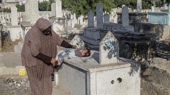 GAZA, PALESTINE - 2022/10/19: Palestinian children from the Kahil family play in front of their home in the Sheikh Shaaban cemetery in Gaza City. There is a battle for space between the living and the dead as the homeless settle in cemeteries. Camelia Kahil, a resident, said that if the dead could speak, they would tell them to get out of there. Due to poverty, they don't have a choice but to live in the cemetery and endure the pungent smell, which they call 