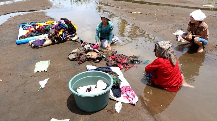 Tiga orang warga mencuci pakaiannya yang masih bisa dipakai setelah sempat terendam banjir.