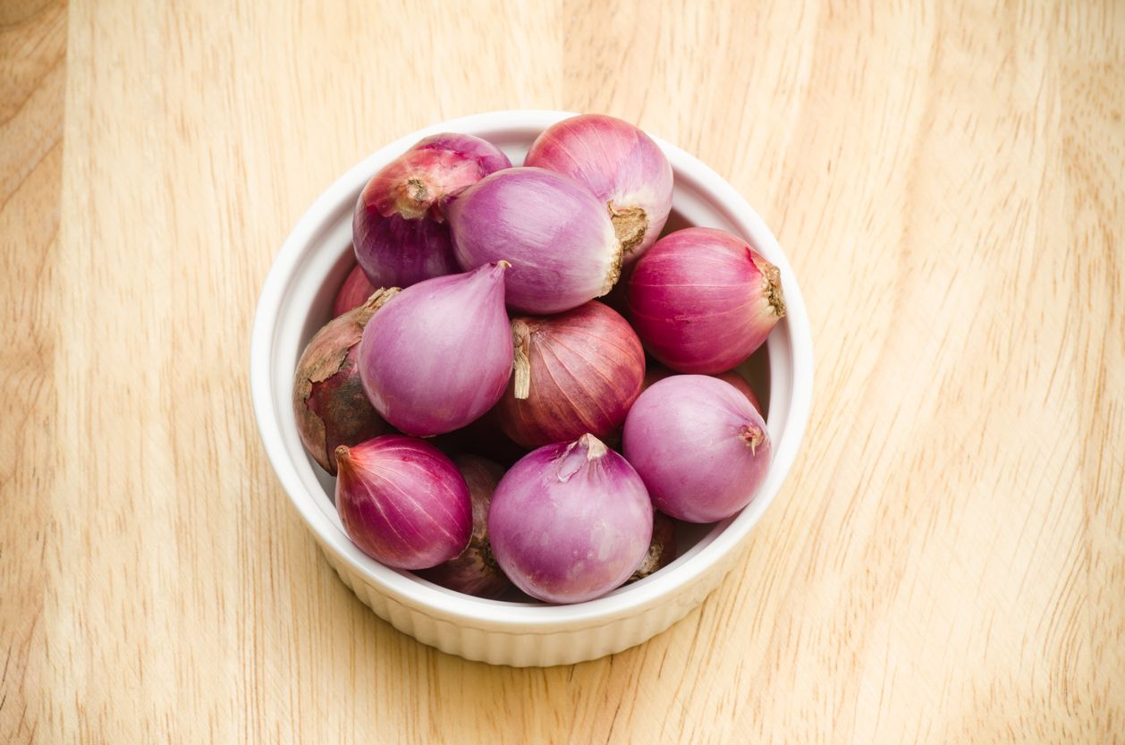 Fresh organic shallots (food ingredient) in the bowl for cooking on wooden background