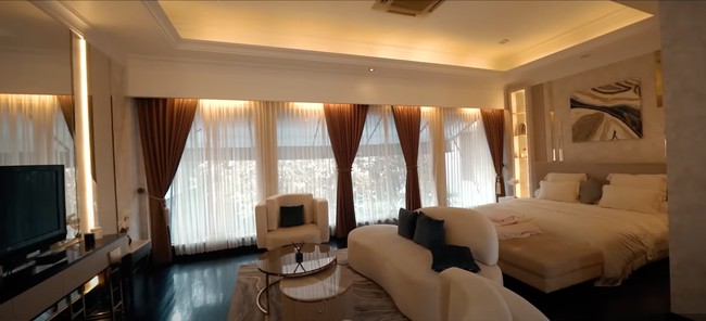 Ruangan kamar tidur di rumah tempat kerja Tasya Farasya itu tampak begitu luas dan mewah dengan lampu berwarna kuning. Bak hotel bintang 5, fasilitas di kamar tersebut juga cukup lengkap. Terdapat sebuah televisi sofa berwarna putih yang diletakkan di depan tempat tidurnya. Foto: YouTube/The Hermansyah A6