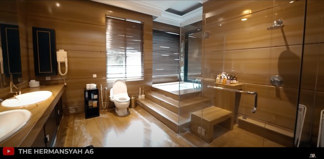 Tak kalah mewah, begini penampakan kamar mandi di rumah tempat kerja Tasya Farasya. Didominasi dengan warna coklat, kamar mandinya itu bak hotel bintang 5 yang luas dan mewah. Beragam fasilitas seperti hair dryer, tempat untuk berendam, dan wastafel tampak tersedia di kamar mandinya itu. Foto: YouTube/The Hermansyah A6