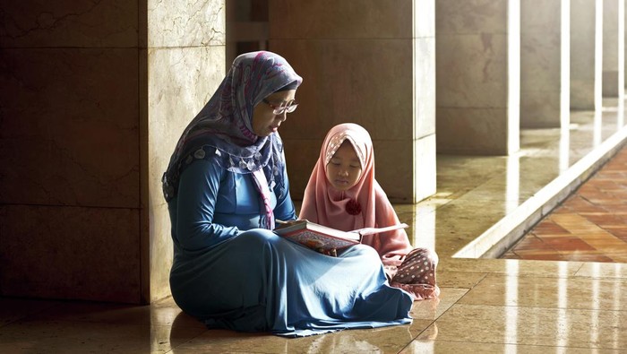 Muslim mother teach her daughter reading koran inside the mosque