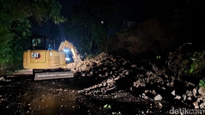 Tampak alat berat sedang membersihkan material longsor di badan jalan.