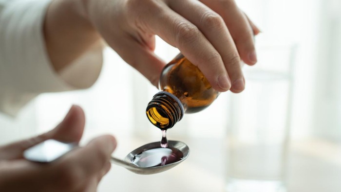 Happy Asia little child girl smiling want to take medicine form mother. Asian kid female waiting to eat drug. Hands of mom pouring cough syrup medicine into clear spoon to daughter.
