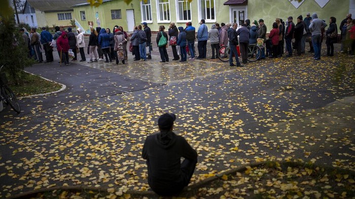 People queue to receive a daily ration of bread in a school in Mykolaiv, Tuesday, Oct. 25, 2022. Mykolaiv residents pick up bread from the only food distribution point in Varvarivka, a Mykolaiv district where thousands of people live. One person is allowed to receive free bread just once in three days. (AP Photo/Emilio Morenatti)