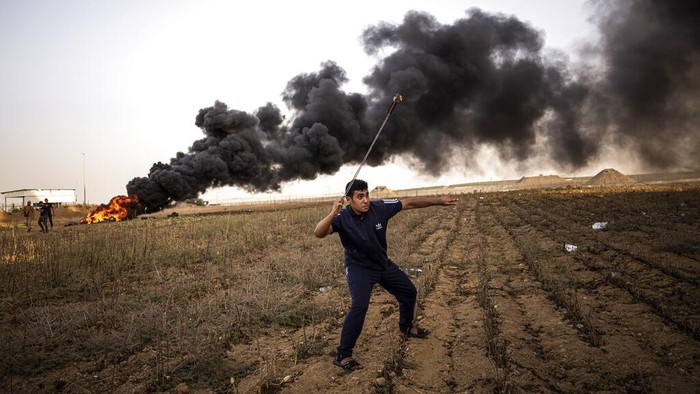 A demonstrator holds a Palestinian flag during a protest against Israeli military raid in the West Bank, along the border fence with Israel, in east of Gaza City, Tuesday, Oct. 25, 2022. The military says Israeli forces have raided a stronghold of an armed group in the West Bank, blowing up an explosives lab and engaging in a firefight. Palestinian health officials say five Palestinians were killed and 20 were wounded. The target of the raid was a group calling itself the Lions' Den, accused by Israel of having killed a soldier and attempting several attacks. (AP Photo/Fatima Shbair)