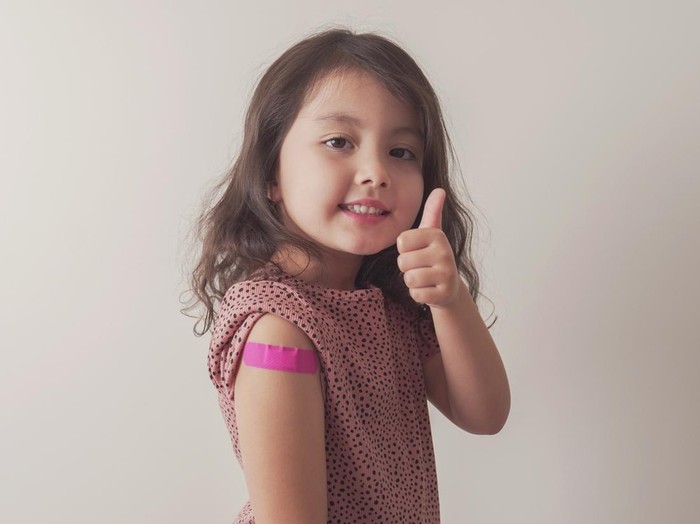 Young mixed Asian girl giving thumb up and showing her arm with pink bandage after got vaccinated or inoculation, child under 12 years old immunization, health concept