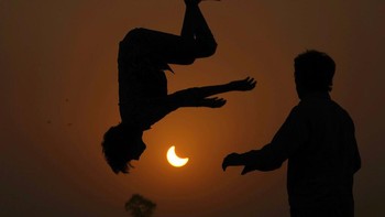 Kecantikan gerhana Matahari parsial terbingkai oleh aktivitas anak-anak yang melompat di atas trampolin di pinggiran Lahore, Pakistan. Foto: AP/Hassan Ammar