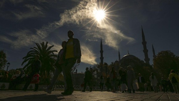 Pejalan kaki berjalan di dekat masjid Sultan Ahmed selama gerhana matahari sebagian di Istanbul, Turki, Selasa (25/10/2022). Sayangnya gerhana matahari sebagian ini tidak dapat disaksikan dari Indonesia menurut Badan Riset dan Inovasi Nasional (BRIN). (AP Photo/Emrah Gurel)  