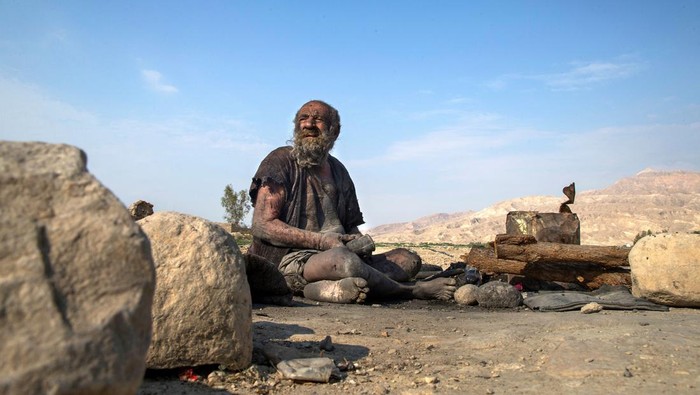 Potret Amou Haji, Pria Paling Kotor di Dunia Meninggal pada Usia 94 Tahun Amou Haji (uncle Haji) smokes from his waterpipe as he sits on the ground on the outskirts of the village of Dezhgah in the Dehram district of the southwestern Iranian Fars province, on December 28, 2018. - Believed to be the worlds dirtiest man, villagers say that Haji's leather-like skin hasn't touched soap and water for more than sixty years. They believe that he decided to live in isolation after suffering from an emotional setback in his youth. (Photo by - / AFP) (Photo by -/AFP via Getty Images)