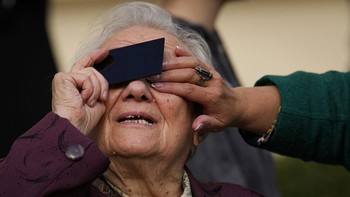 Seorang wanita lansia di Bucharest, Rumania, tak mau ketinggalan menonton momen langka ini. Ia melihat gerhana Matahari melalui filter. Foto: AP/Victor Berezkin