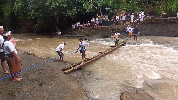 Warga Banjar Bongan Gede yang hendak sembahyang Pagerwesi di Pura Beji setempat harus melalui titi (jembatan kecil) dari bambu atau digendong saat menyeberangi sungai atau Tukad Yeh Panan, Rabu (26/10/2022). (Istimewa)
