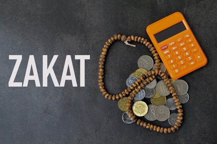 Top view of calculator, prayer beads and coins over black background written with ZAKAT