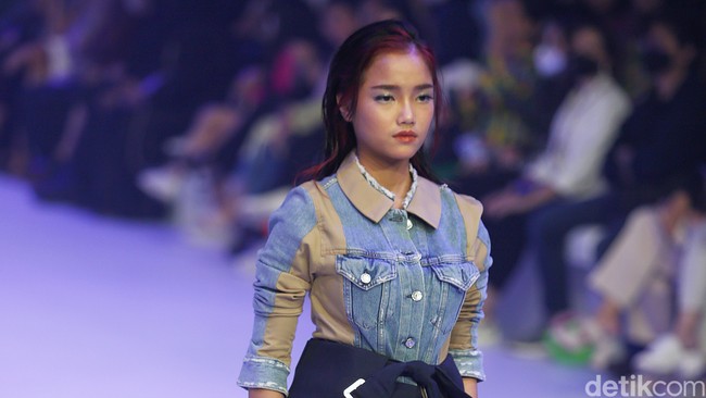 Fuji memakai skirt denim daur ulang, blazer yang diikat di pinggang dan celana pendek potongan longgar. Penampilan Fuji yang menjadi model langsung menjadi sorotan. Ia catwalk dengan rasa percaya diri dan tatapan yang tajam. Fuji berjalan sambil memasukkan tangan ke dalam saku.  Foto: Agung Pambudhy/Detikcom.