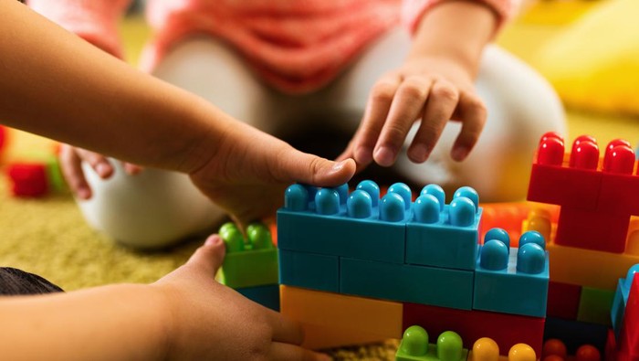 Close-up of  two creative kids building something with plastic blocks on the floor.