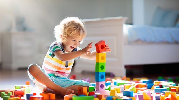 Child playing with colorful toy blocks. Kids play. Little boy building tower of block toys sitting on dark floor in sunny white bedroom. Educational game for baby and toddler. Children build toy house