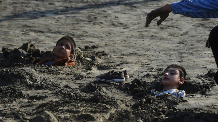 Orang Tua di Pakistan Ramai 'Menanam' Anak Dalam Pasir Relatives prepare to cover a boy with sand in a beach with the believe that exposure during a solar eclipse will heal his illness, in Karachi on October 25, 2022. (Photo by Asif HASSAN / AFP) (Photo by ASIF HASSAN/AFP via Getty Images)