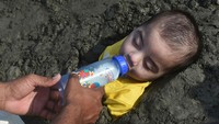 Orang tua memberikan susu pada anaknya yang tertidur pulas saat pengobatan dengan paparan gerhana matahari di pasir pantai Karachi. Asif Hassan/AFP/Getty Images