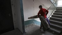 Seorang warga mengevakuasi karpet dan barang-barang lainnya dari apartemennya yang rusak dirudal Rusia.