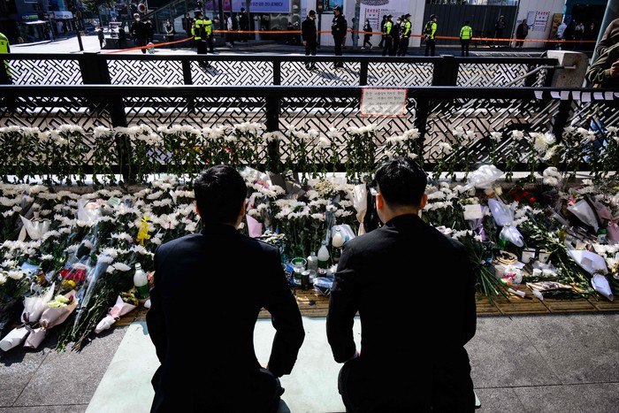 1244371470 Two men kneel down to pay tribute at a makeshift memorial outside a subway station in the district of Itaewon in Seoul on October 31, 2022, two days after a deadly Halloween surge in the area. (Photo by ANTHONY WALLACE / AFP) (Photo by ANTHONY WALLACE/AFP via Getty Images)
