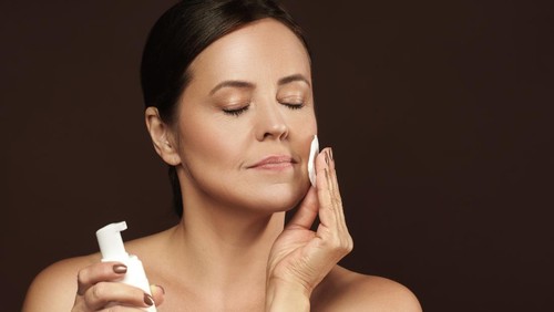 Portrait of a beautiful middle aged woman with a cotton pad and bottle of cleansing liquid