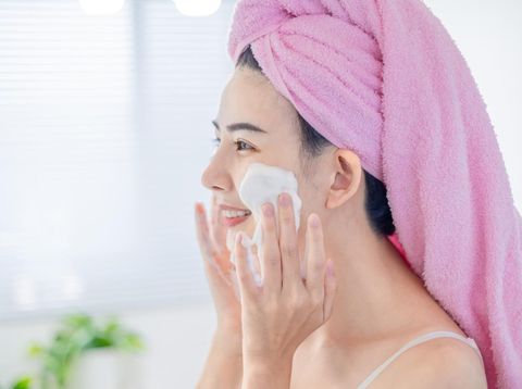 asian beauty woman with towel on head is cleaning her face by facial cleanser in the bathroom