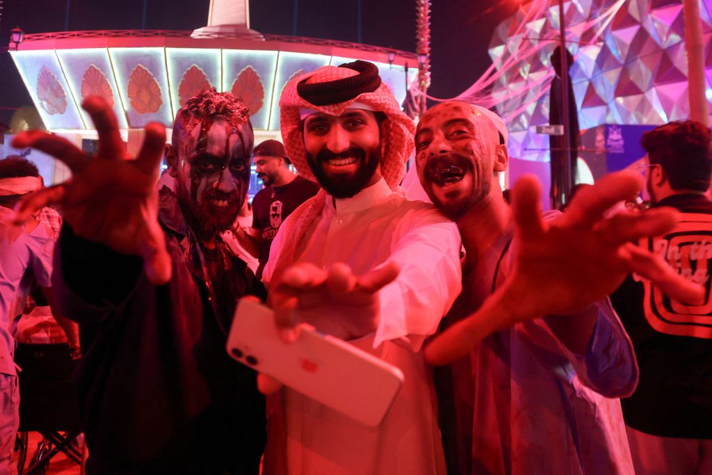 A Saudi man takes a photo with people dressed in costumes to celebrate Halloween during 