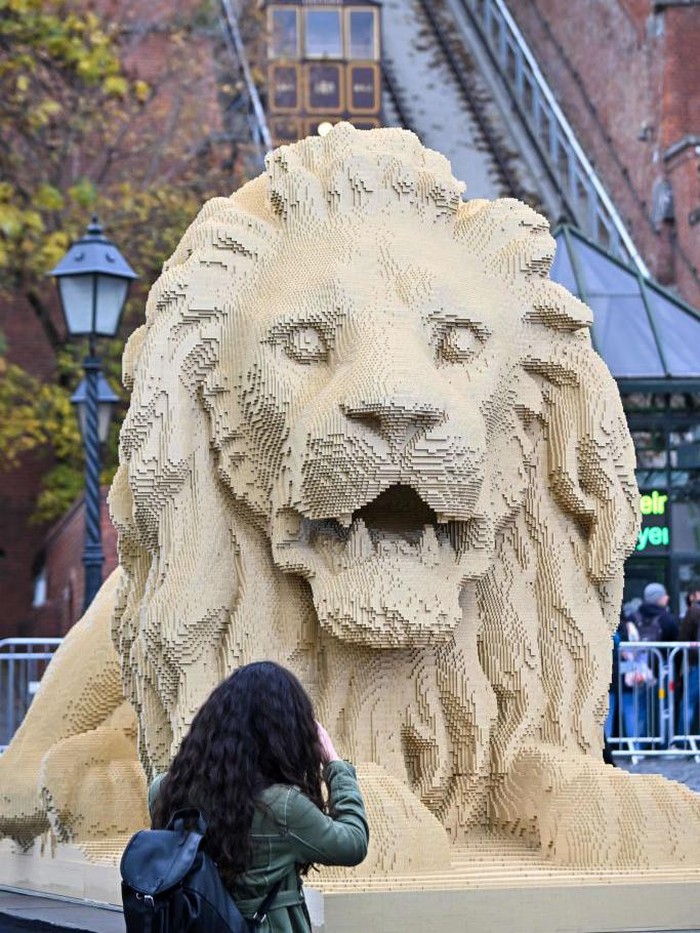 Tourists pose for photos in front of a giant Lego lion statue, a replica of one of the lion statues of the oldest bridge of Hungary - the Chain Bridge - in Budapest, on October 28, 2022. - The replica of the lion statues of the oldest bridge of Hungary, the Szechenyi Lanchid, was completed with 850 thousand Lego bricks in 560 hours by official Lego master builder and visual artist Balazs Doczy. The Lego lion was made on a scale of 1:1, the Lego statue is 5,80 meters long, 1,70 meters wide, 2,45 meters tall and weighs 1,3 tons. (Photo by ATTILA KISBENEDEK / AFP) (Photo by ATTILA KISBENEDEK/AFP via Getty Images)