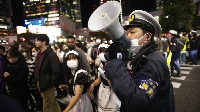 Perayaan Halloween di Tokyo Dijaga Ketat Polisi, Cegah Insiden Itaewon Police officers urge pedestrians in costumes to keep moving through the famed scramble intersection of Tokyo's Shibuya entertainment district during Halloween festivities, Monday, Oct. 31, 2022. (AP Photo/Hiro Komae)