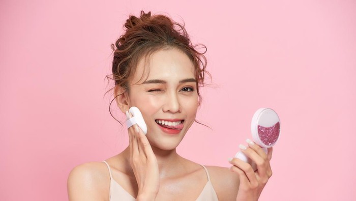 Young woman putting powder on her face