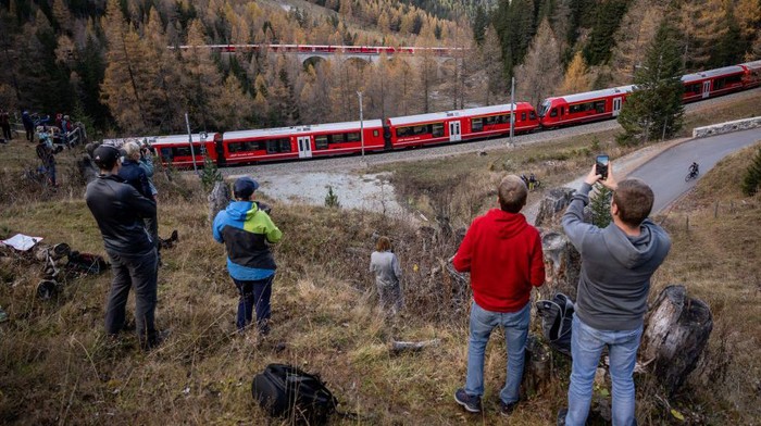 Members of the public capture images as a 1910-metre-long train with 100 cars passes near Bergun, on October 29, 2022, during a record attempt by the Rhaetian Railway (RhB) of the World's longest passenger train, to mark the Swiss railway operator's 175th anniversary. - The record attempt is carried out on the Albula Line, from Preda to Thusis, crossing one of the most spectacular railways in the world, recognised as a Unesco World Heritage Site. (Photo by Fabrice COFFRINI / AFP) (Photo by FABRICE COFFRINI/AFP via Getty Images)