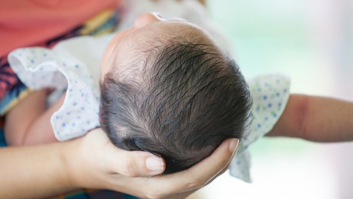Mother holding head of her newborn baby girl in hand with love