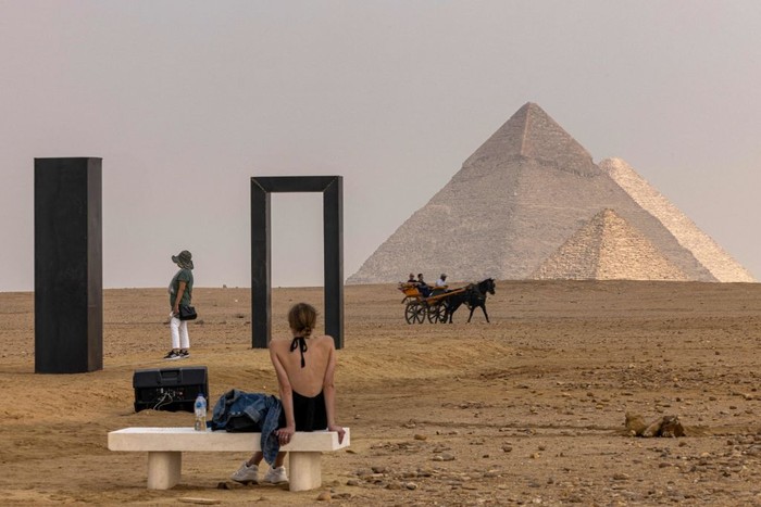 A woman looks on while a horse-drawn carriage passes by Italian artist Emilio Ferros artwork installation Portal of Light at the Giza pyramids necropolis during the second edition of the Art DÉgypte exhibition Forever is Now on October 27, 2022. - - RESTRICTED TO EDITORIAL USE - MANDATORY MENTION OF THE ARTIST UPON PUBLICATION - TO ILLUSTRATE THE EVENT AS SPECIFIED IN THE CAPTION (Photo by Khaled DESOUKI / AFP) / RESTRICTED TO EDITORIAL USE - MANDATORY MENTION OF THE ARTIST UPON PUBLICATION - TO ILLUSTRATE THE EVENT AS SPECIFIED IN THE CAPTION / RESTRICTED TO EDITORIAL USE - MANDATORY MENTION OF THE ARTIST UPON PUBLICATION - TO ILLUSTRATE THE EVENT AS SPECIFIED IN THE CAPTION (Photo by KHALED DESOUKI/AFP via Getty Images)
