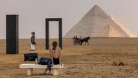Seorang wanita melihat saat kereta kuda melewati instalasi karya seni seniman Italia Emilio Ferro Portal of Light di pekuburan piramida Giza selama edisi kedua pameran Art DÉgypte Forever is Now. Khaled Desouki/AFP/Getty Images
