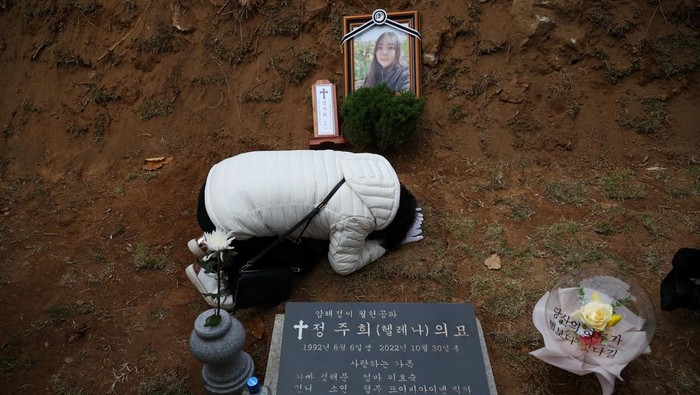Potret Pilu Pemakaman Korban Halloween Itaewon Lee Hyo-sook, 61, mother of Jung Joo-hee, 30, who was one of the victims of a crowd crush that happened during Halloween festivities, grieves next to her daughter's grave in Namyangju, South Korea, November 3, 2022. REUTERS/Kim Hong-Ji